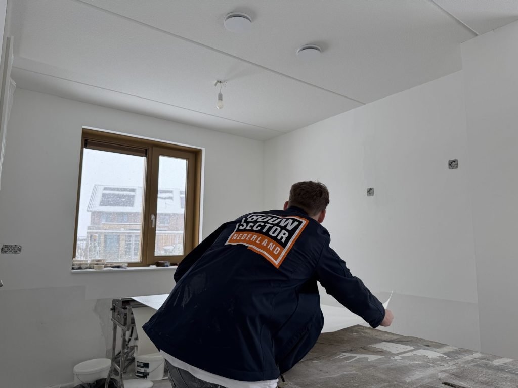 Behanger in werkjas van Bouwsector Nederland legt een baan vlies op de plaktafel in een nieuwbouwkamer