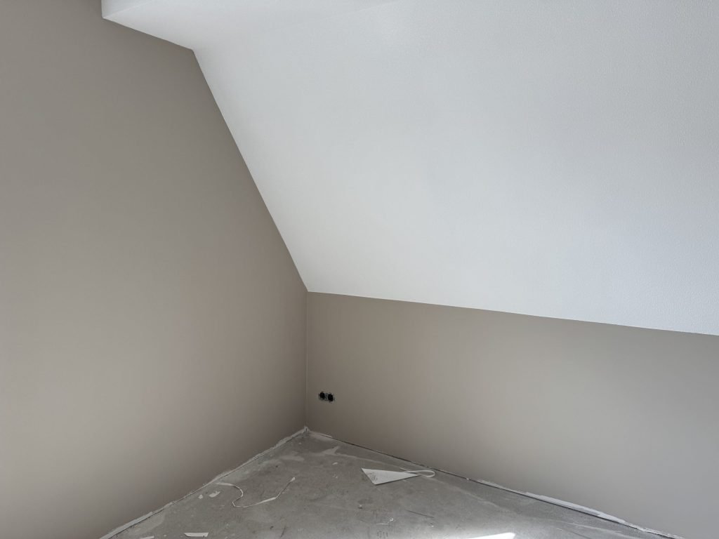Zolderkamer met een witte schuine wand en rechte wanden in een zachte beige tint
