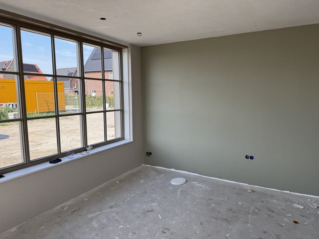 Nieuwbouwkamer met een egaal gesausde wand in grijsgroen naast een groot raam