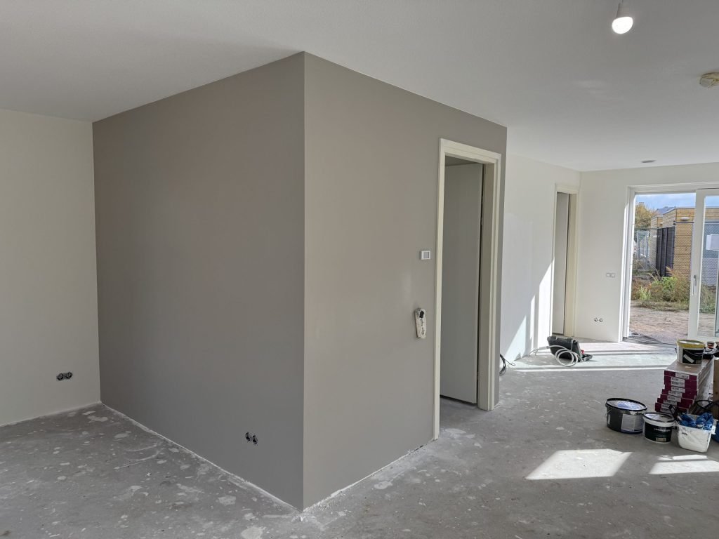 Pas gesausde grijze wand in een nieuwbouwwoning met verfemmers op de vloer bij de tuindeuren
