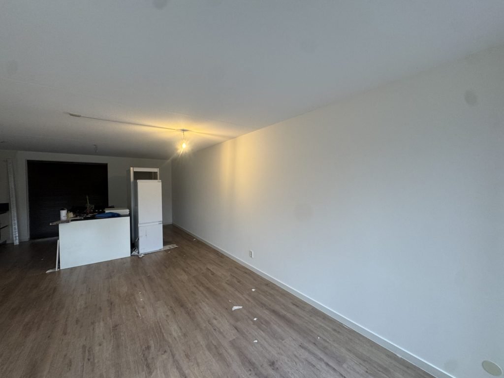 Lange, gladde witte wand in een woonkamer met laminaat en een keukenblok