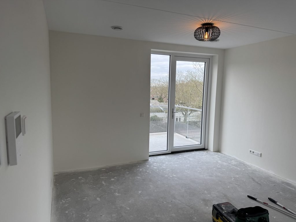Lege nieuwbouwkamer met lichte wanden en openslaande deuren naar een balkon