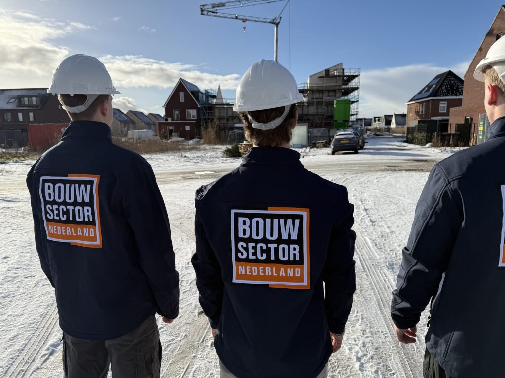 Drie vakmensen van Bouwsector Nederland met witte helm in een besneeuwde nieuwbouwwijk met een bouwkraan